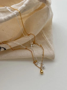 Detail of silver and gold teardrop pendant necklaces on a natural linen pouch