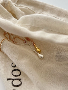 Detail of silver and gold solid droplet pendants on a textured canvas bag background