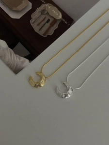 Detail of moon necklaces with hammered texture and zircon in gold and silver