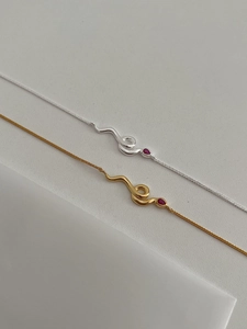Nahaufnahme von Schlangenketten in Gold und Silber mit roten Tropfen-Edelsteinen