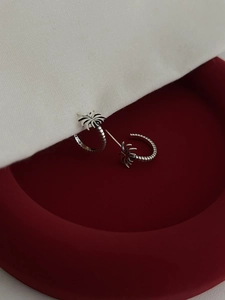 Macro shot of S925 silver palm tree earrings on red velvet and white fabric