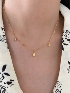 Detailed close-up of a minimalist gold teardrop pendant necklace worn by a model