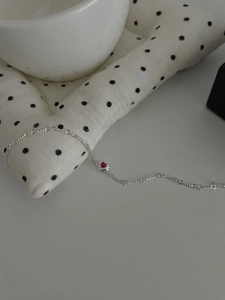 Detailed macro of a silver chain bracelet featuring a tiny red heart gemstone inlay