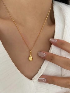 Close-up of a minimalist gold waterdrop pendant necklace worn with a white cardigan