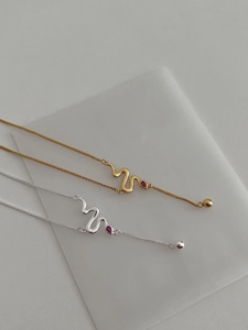 Detail of silver and gold snake necklaces with red ruby gemstone accents on matte stand