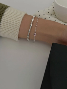 Detail of layered S925 silver bracelets with a red heart-shaped gemstone on model