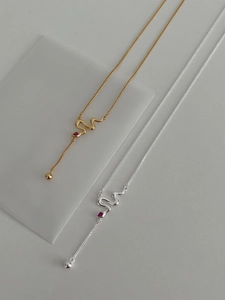 Macro view of gold and silver snake necklaces with a red teardrop gemstone detail