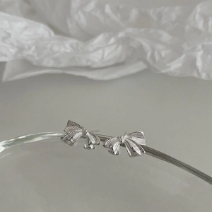 Boucles d'oreilles nœud argentées avec texture ruban sur support d'affichage minimaliste