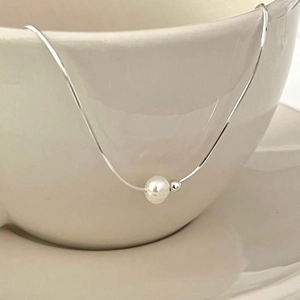 Minimalist silver snake chain necklace with natural pearl on a ceramic cup edge