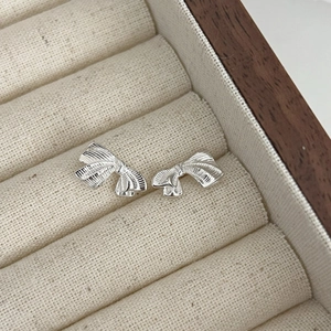Boucles d'oreilles nœud argentées avec texture 3D présentées sur un coussin à bijoux