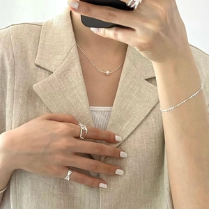 Close-up of minimalist silver snake chain with white pearl and layered rings on model