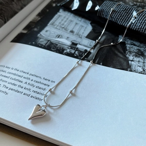 Silver heart pendant necklace with beaded snake chain layered on a stylish magazine