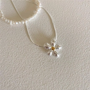 Macro shot of silver flower pendant with gold center on a delicate snake chain