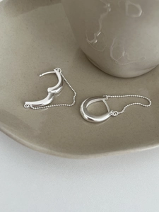Gros plan de boucles d'oreilles U en argent poli avec fines chaînes à billes sur plateau