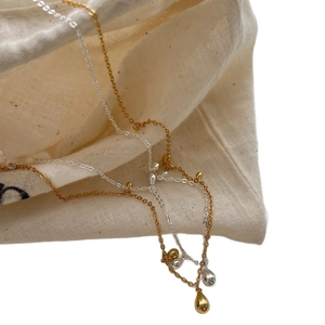 Minimalist 925 silver and gold teardrop pendant necklaces on a natural linen bag