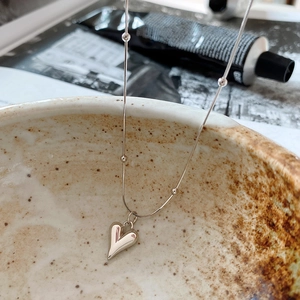 Macro shot of silver heart pendant on a bead snake chain over a ceramic bowl