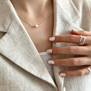 Detail shot of a minimalist natural pearl necklace and geometric silver ring on a model