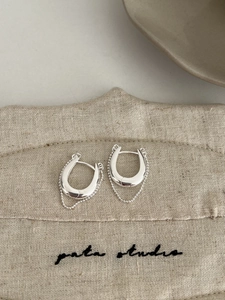 Détail de boucles d'oreilles en U argentées avec chaînes à billes sur lin beige