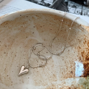 Silver heart pendant necklace with beaded snake chain on a textured ceramic bowl