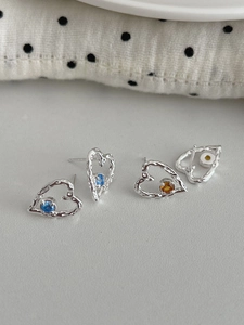 Detail of silver heart earrings with blue and amber zircons on a polka dot background