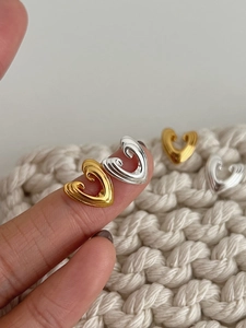 Detailed view of 3D heart-shaped silver and gold stud earrings on a knitted surface