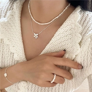 Detail of S925 silver flower necklace and pearl jewelry set worn by model on white knit