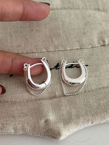 Gros plan détaillé de boucles d'oreilles argentées en U avec fine chaîne à billes polie
