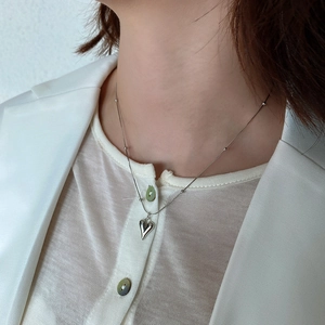 Silver heart pendant on a beaded chain necklace worn by a model in white attire
