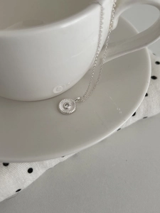 Detail der S925 Silbernen Sonnenblumen-Kette mit Zirkonia an einer weißen Tasse