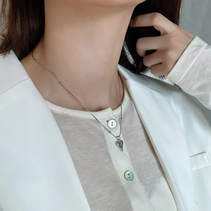 Close-up of minimalist silver heart pendant necklace on model wearing white blazer