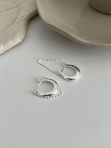 Gros plan de boucles d'oreilles en U argentées avec fine chaîne à billes sur fond beige