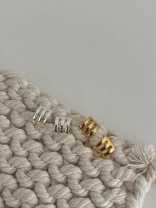 Macro shot of minimalist silver and gold triple-claw stud earrings on textured knit fabric