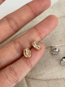 Macro shot of tulip-shaped gold stud earrings with teardrop zircon held by hand