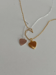 Detail of two layered heart pendant necklaces in polished gold and silver finishes