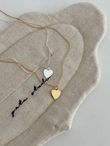 Detail showing gold and silver S925 heart pendant necklaces on a natural linen fabric bag