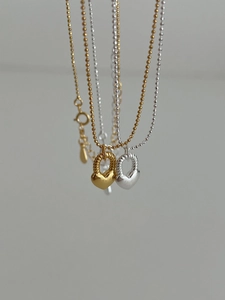 Dettaglio macro di ciondoli a cuore in oro e argento su collane a sfere con anello inciso