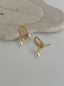 Detail view of retro gold twist metal earrings featuring elegant white pearls on fabric