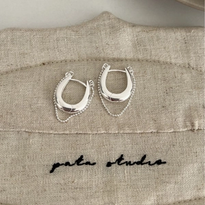 Boucles d'oreilles en U argentées polies avec chaînes à billes sur fond de lin