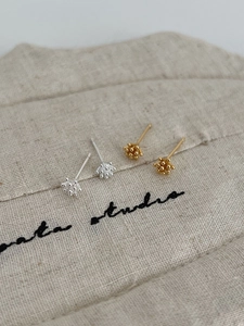 Detailed view of silver and gold pine cone stud earrings on natural linen background
