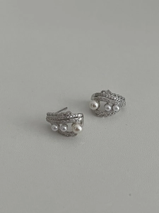 Macro shot of silver pearl earrings with multilayered zircon curves on grey background