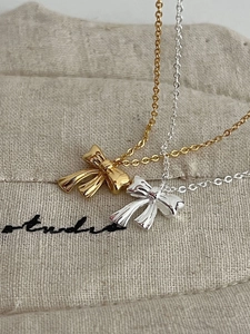 Detail of silver and gold bow necklaces on a beige linen pouch showing refined metal textures