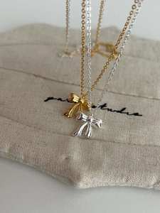 Detailed view of silver and gold bow pendants hanging on a beige linen jewelry pouch