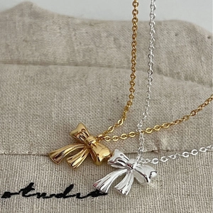 Minimalist S925 silver bow necklaces in gold and silver finish on linen bag