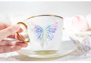 Gros plan d'une tasse en céramique avec papillon iridescent et poignée dorée élégante