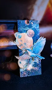 Celestial bookmark detail featuring starry planets and bird with silk ribbon on dark piano