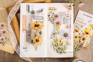 Dettaglio flat lay di adesivi floreali vintage e carta artigianale su un taccuino bianco