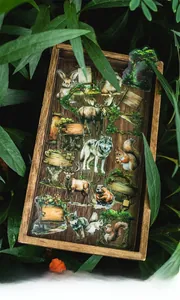 Forest animal themed stickers pack on wooden tray surrounded by lush green leaves