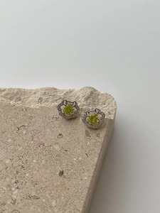 Macro detail of silver lock stud earrings with green gemstone and diamond halo petals