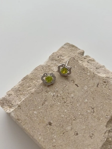 Detailed macro view of S925 silver stud earrings with a green gemstone and diamond halo