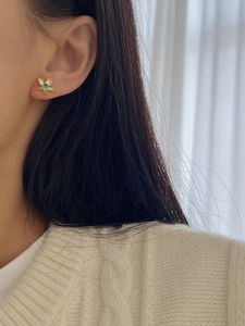 Détail d'une boucle d'oreille fleur dorée avec pierre bleue portée sur l'oreille